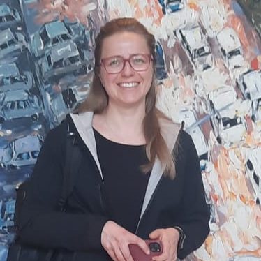 Bild von Frau Dr. Sarah Scholze vor einer bunten, abstrakten Hintergrundmalerei.