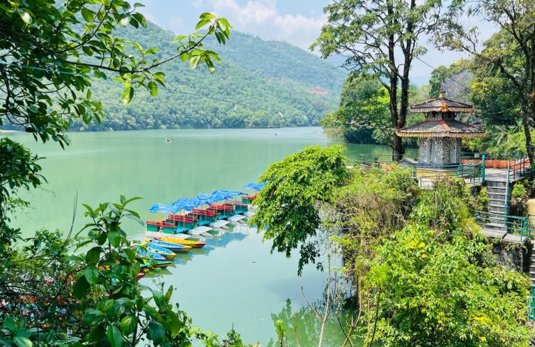 Blick auf Phewa-See in Nepal mit bunten Booten und grüner Landschaft im Hintergrund.