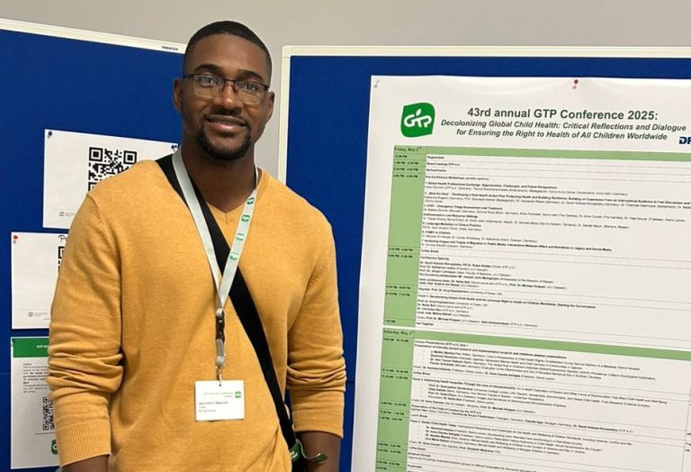 Dr. Jeronimo Sequice steht neben einem Plakat der GTP Tagung. 